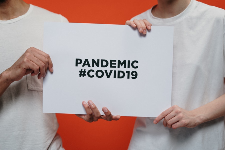 Two people in white t-shirs holding sign saying Pandemic #Covid-19. Photo by cottonbro from Pexels