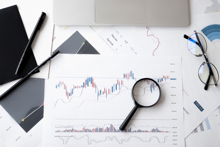 A desk with a graph of stocks and shares with a magnifiying glass and some glasses